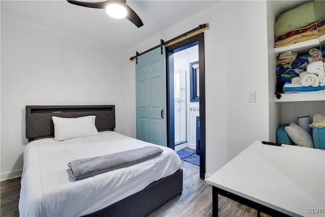 bedroom featuring a ceiling fan, wood finished floors, baseboards, ornamental molding, and a barn door