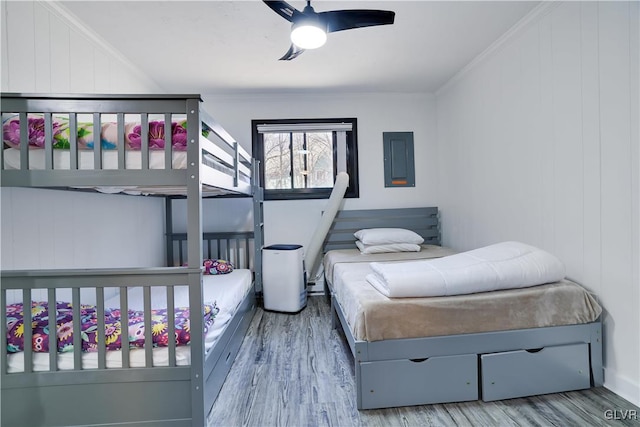 bedroom with electric panel, wood finished floors, ornamental molding, and ceiling fan