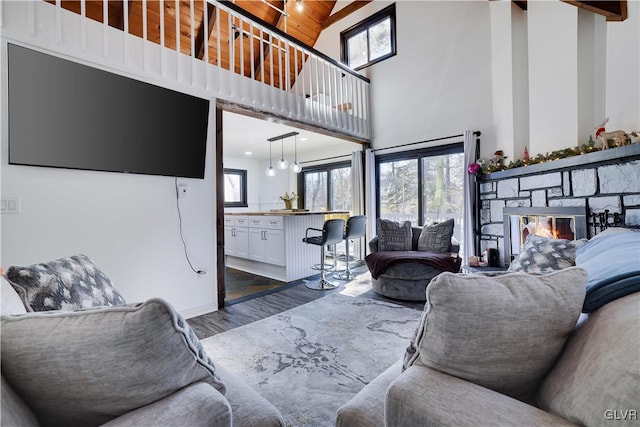 living area featuring dark wood finished floors, a stone fireplace, wood ceiling, and high vaulted ceiling