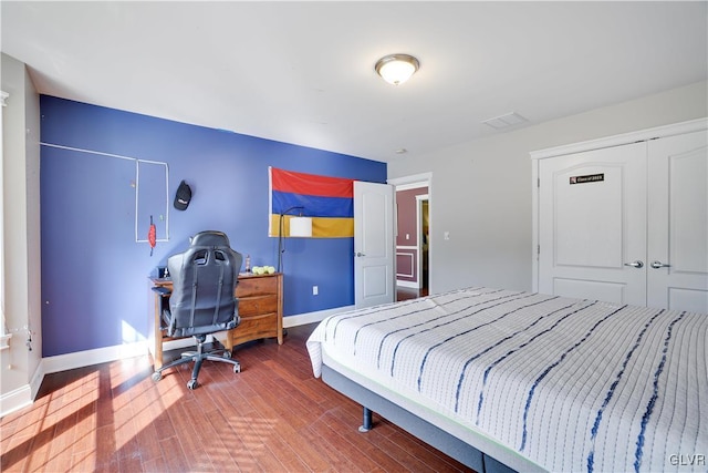 bedroom with a closet, wood finished floors, visible vents, and baseboards