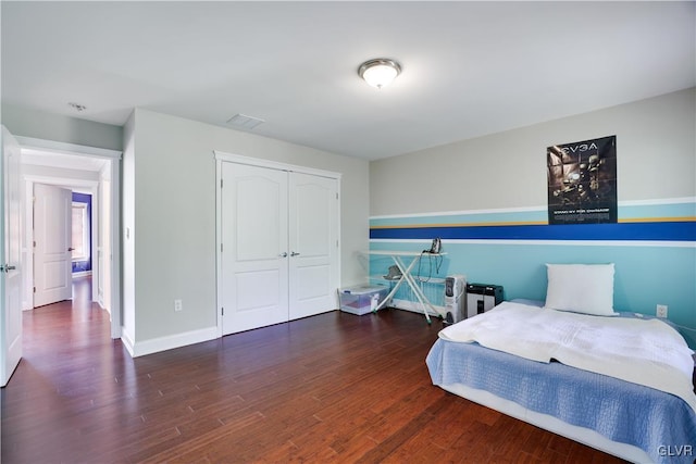 bedroom with a closet, wood finished floors, visible vents, and baseboards