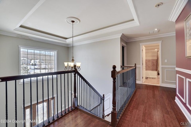 hall with a chandelier, a raised ceiling, an upstairs landing, and wood finished floors