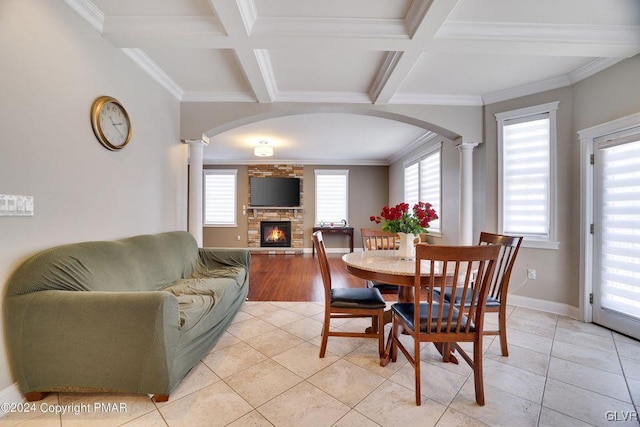 dining space featuring arched walkways, a stone fireplace, coffered ceiling, and ornate columns