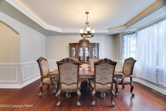 dining room with an inviting chandelier, arched walkways, a raised ceiling, and hardwood / wood-style floors