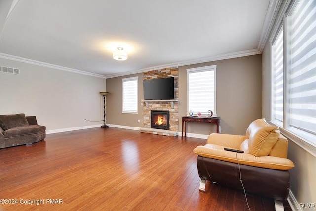 living area with a fireplace, wood finished floors, visible vents, baseboards, and crown molding