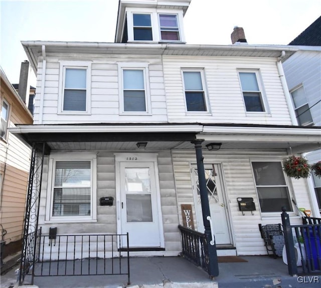 townhome / multi-family property with a porch, a chimney, and a fenced front yard