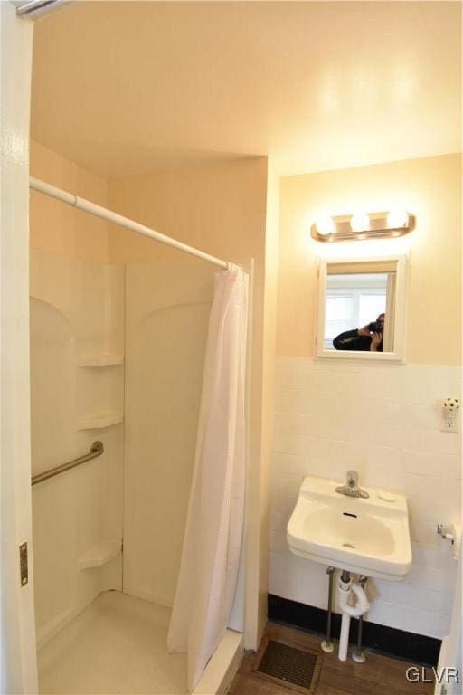 full bathroom with a stall shower, tile walls, and a sink