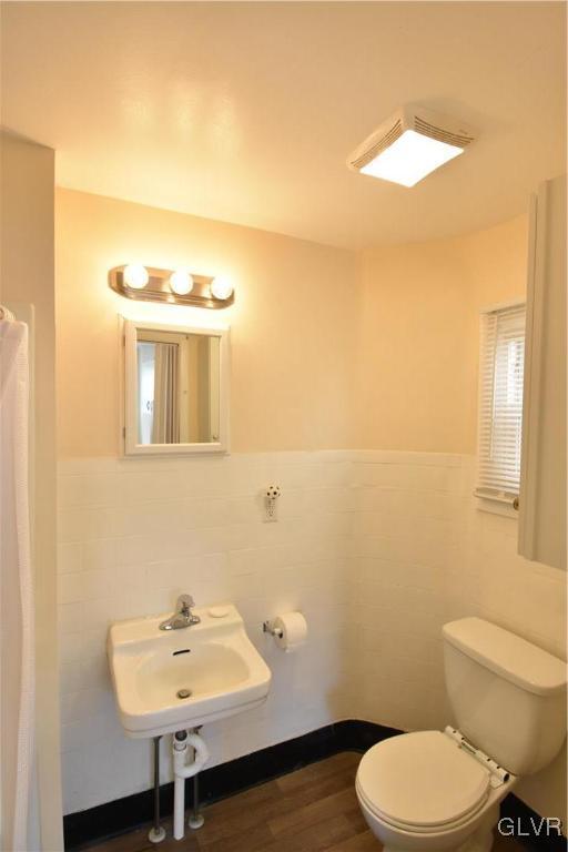 bathroom with tile walls, toilet, wainscoting, a sink, and wood finished floors