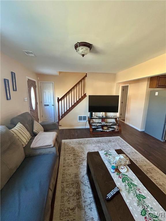 living room with dark wood-type flooring, visible vents, baseboards, and stairs