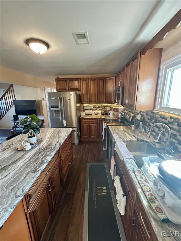 kitchen with decorative backsplash, dark wood-style floors, light stone counters, stainless steel appliances, and a sink