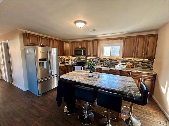 kitchen with tasteful backsplash, stainless steel appliances, dark wood-style flooring, and a kitchen breakfast bar