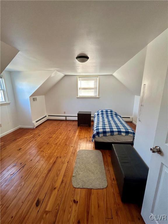 unfurnished bedroom featuring a baseboard heating unit, lofted ceiling, wood-type flooring, and multiple windows