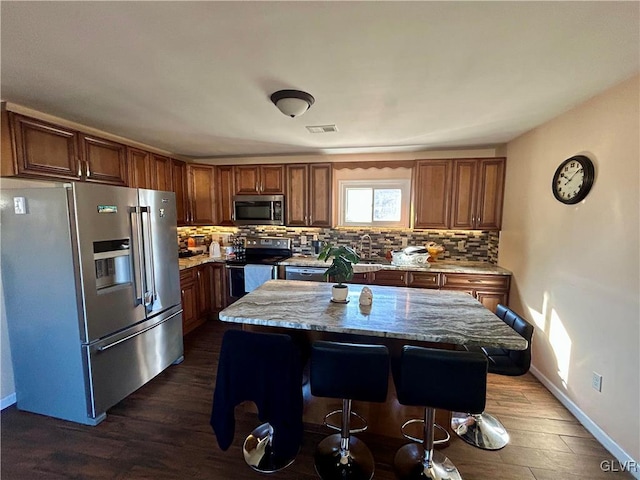 kitchen with visible vents, decorative backsplash, dark wood-style floors, a breakfast bar, and stainless steel appliances