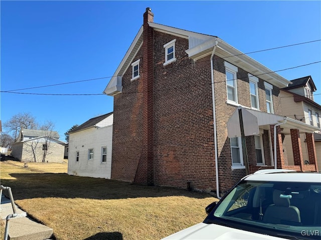 view of side of property featuring brick siding, a lawn, and a chimney