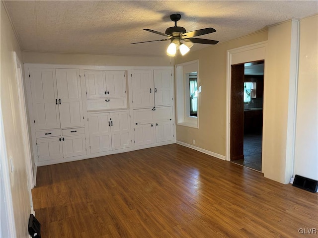 unfurnished bedroom with dark wood-style flooring, two closets, ceiling fan, a textured ceiling, and baseboards