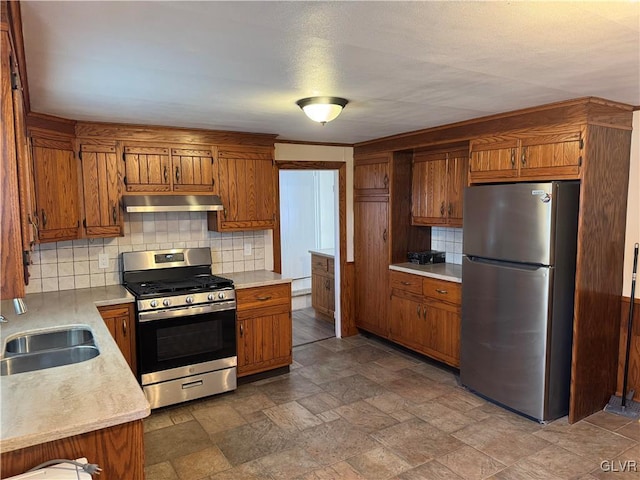 kitchen with appliances with stainless steel finishes, brown cabinetry, a sink, and under cabinet range hood