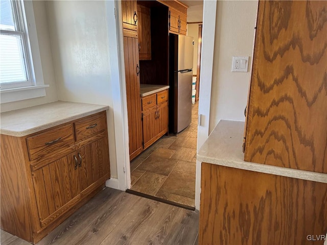 kitchen featuring dark wood-style floors, light countertops, brown cabinetry, and freestanding refrigerator