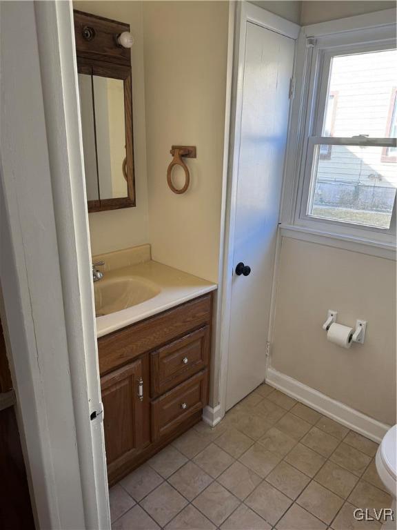 half bathroom with baseboards, vanity, and toilet