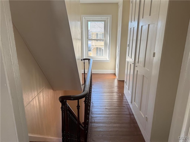 corridor with dark wood-type flooring, baseboards, and an upstairs landing