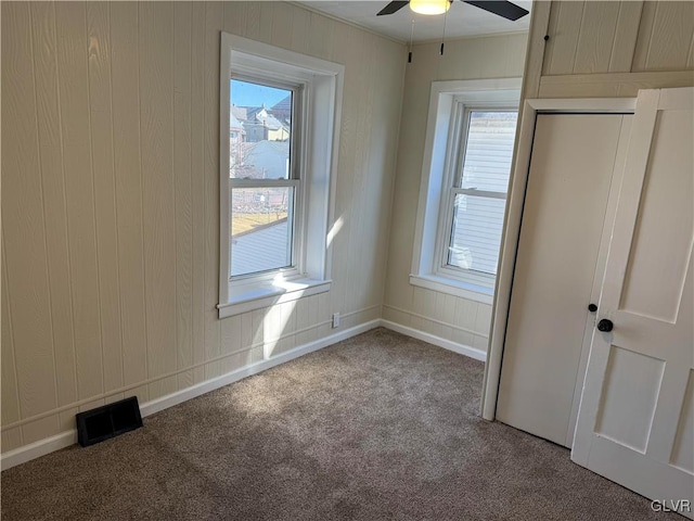 unfurnished bedroom featuring carpet, crown molding, visible vents, a ceiling fan, and baseboards