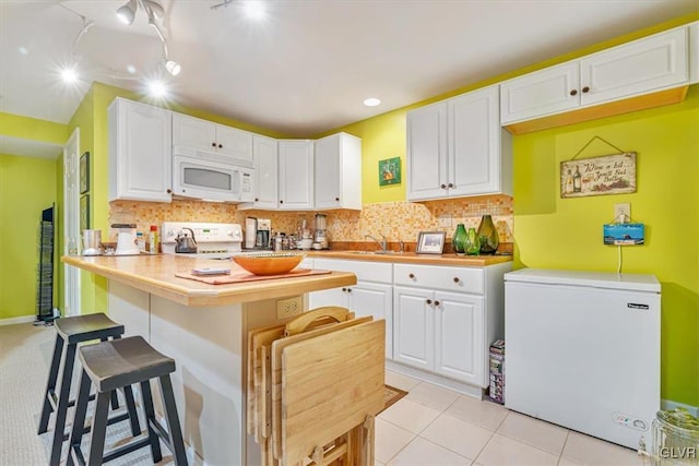 kitchen featuring white appliances, decorative backsplash, white cabinets, and a kitchen breakfast bar