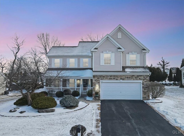 traditional-style house with stone siding, a porch, an attached garage, and aphalt driveway