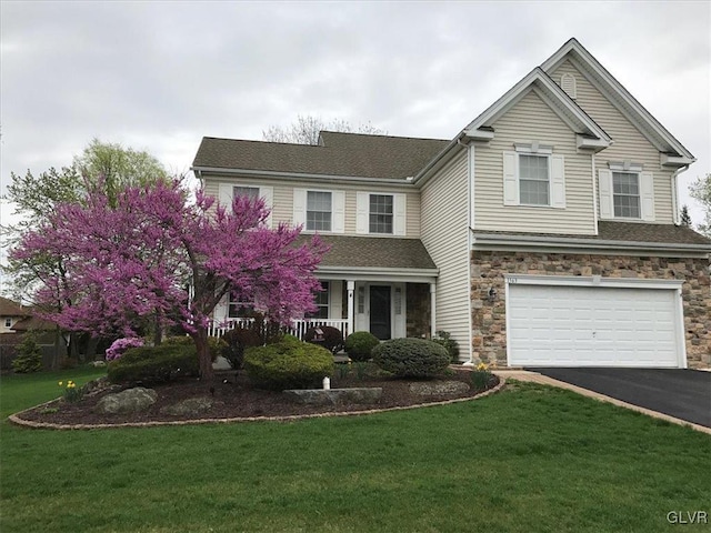 traditional-style home with driveway, stone siding, a porch, an attached garage, and a front lawn