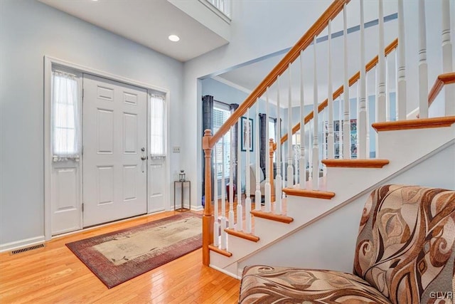 foyer entrance featuring wood finished floors, visible vents, baseboards, stairs, and crown molding