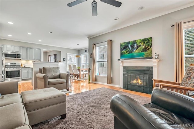 living area featuring light wood finished floors, recessed lighting, ceiling fan, a tile fireplace, and baseboards