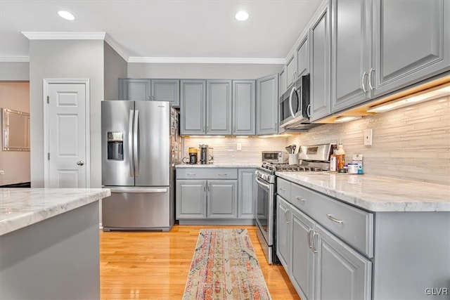 kitchen featuring light wood-style flooring, stainless steel appliances, gray cabinets, tasteful backsplash, and crown molding