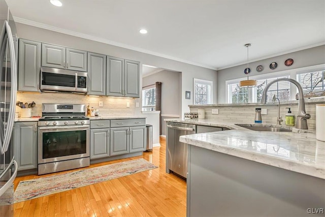 kitchen featuring appliances with stainless steel finishes, light stone countertops, gray cabinets, crown molding, and a sink