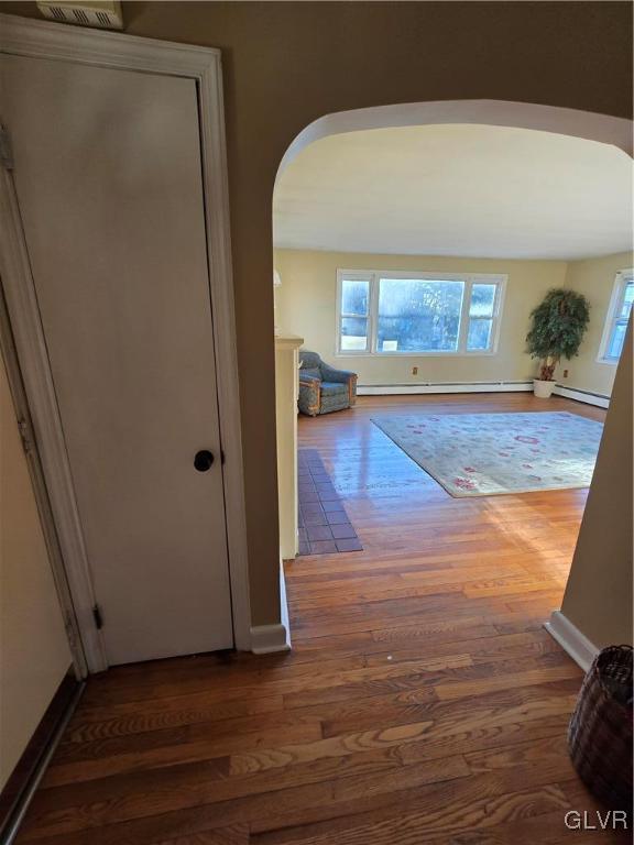 hallway featuring wood finished floors, arched walkways, and a baseboard radiator