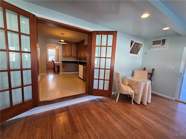 interior space with a baseboard heating unit, baseboards, a wall unit AC, wood finished floors, and arched walkways