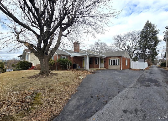 view of front facade with brick siding, a chimney, aphalt driveway, and fence