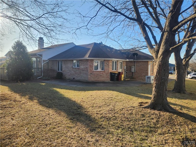 back of property with central air condition unit, brick siding, a chimney, and a lawn