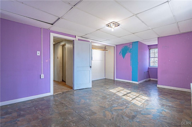 spare room featuring baseboards and a drop ceiling