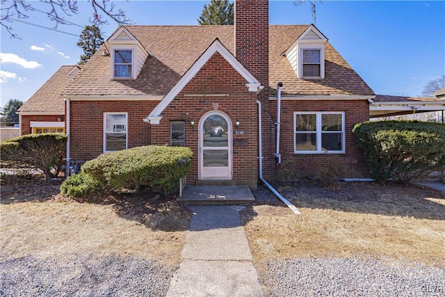 view of front facade with brick siding, a chimney, and a shingled roof