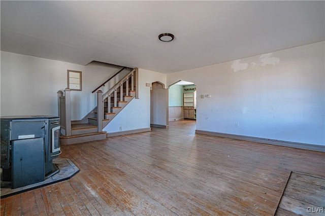 unfurnished living room featuring stairway, baseboards, a wood stove, arched walkways, and wood-type flooring