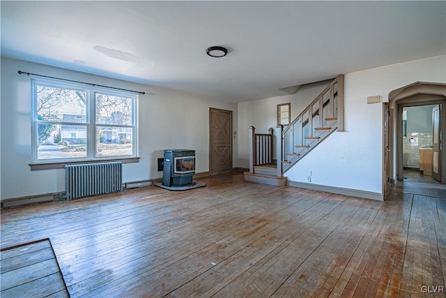 unfurnished living room featuring hardwood / wood-style floors, radiator, baseboards, a wood stove, and stairs