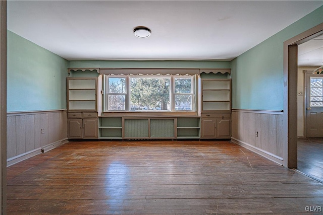 empty room with hardwood / wood-style floors, radiator heating unit, and a wainscoted wall