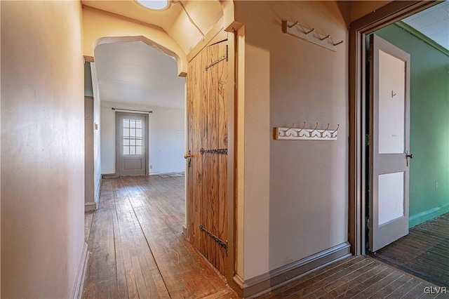 corridor featuring hardwood / wood-style flooring, baseboards, and arched walkways