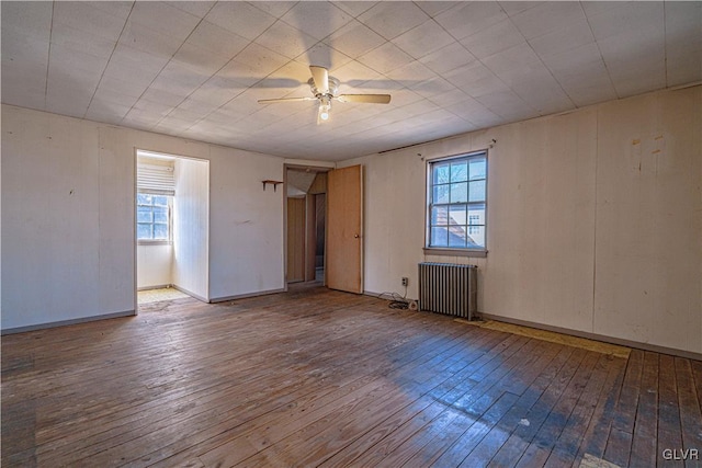 unfurnished room with a wealth of natural light, wood-type flooring, ceiling fan, and radiator heating unit