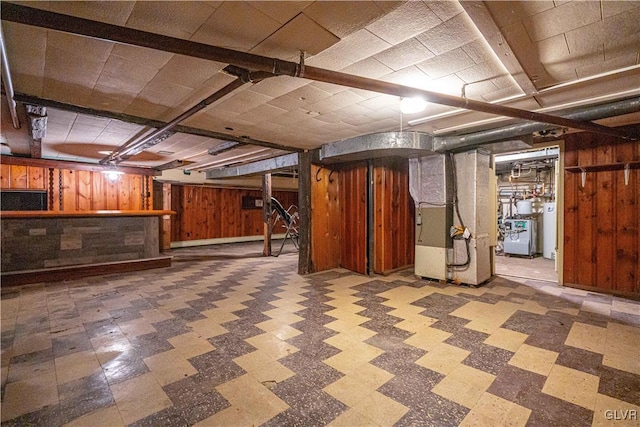 finished basement featuring tile patterned floors, wooden walls, water heater, and a bar