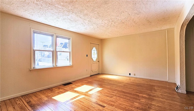 unfurnished room with visible vents, baseboards, wood finished floors, arched walkways, and a textured ceiling