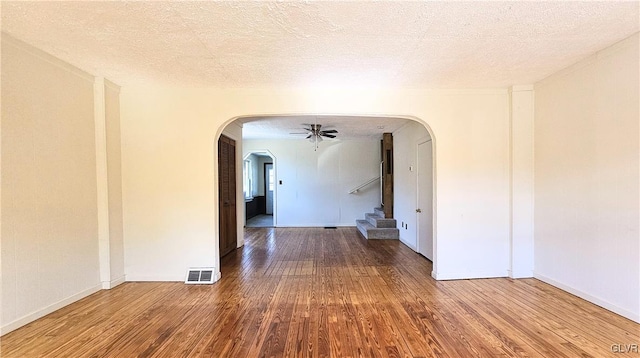 unfurnished room with visible vents, wood finished floors, arched walkways, a textured ceiling, and a ceiling fan