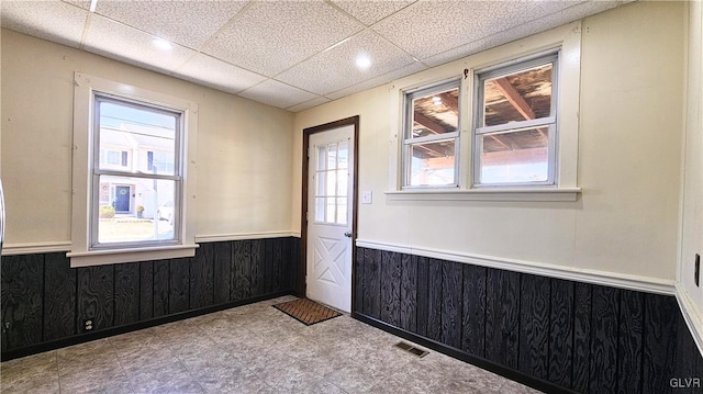 empty room with light floors, visible vents, a wainscoted wall, a drop ceiling, and wood walls