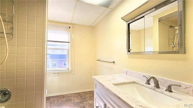 bathroom featuring stone finish floor, vanity, a shower, and baseboards