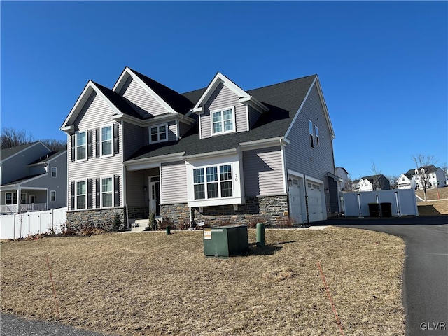 craftsman house featuring stone siding, driveway, a garage, and fence