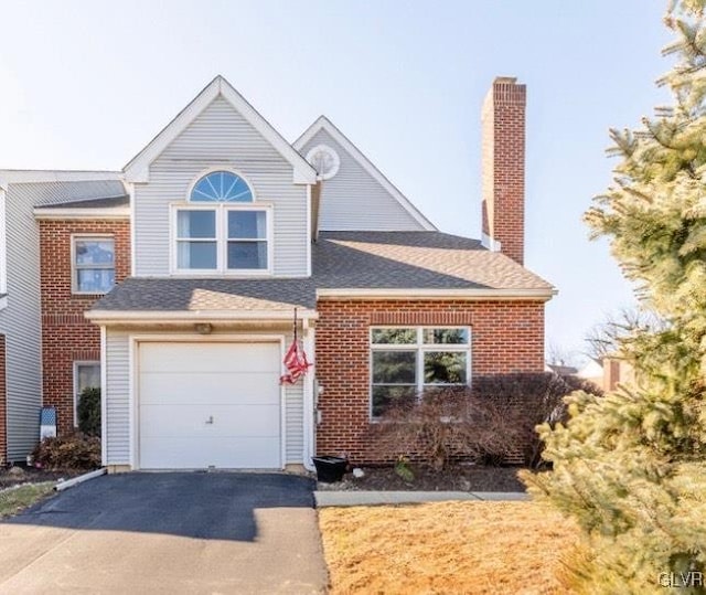 traditional home featuring a shingled roof, brick siding, driveway, and a chimney