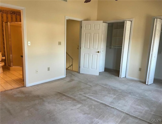 unfurnished bedroom featuring carpet, baseboards, ensuite bath, tile patterned flooring, and a closet